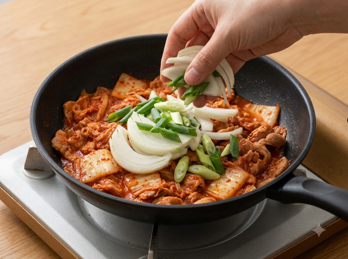 Cipolle affettate e cipollotti aggiunti nella pentola sopra il kimchi.