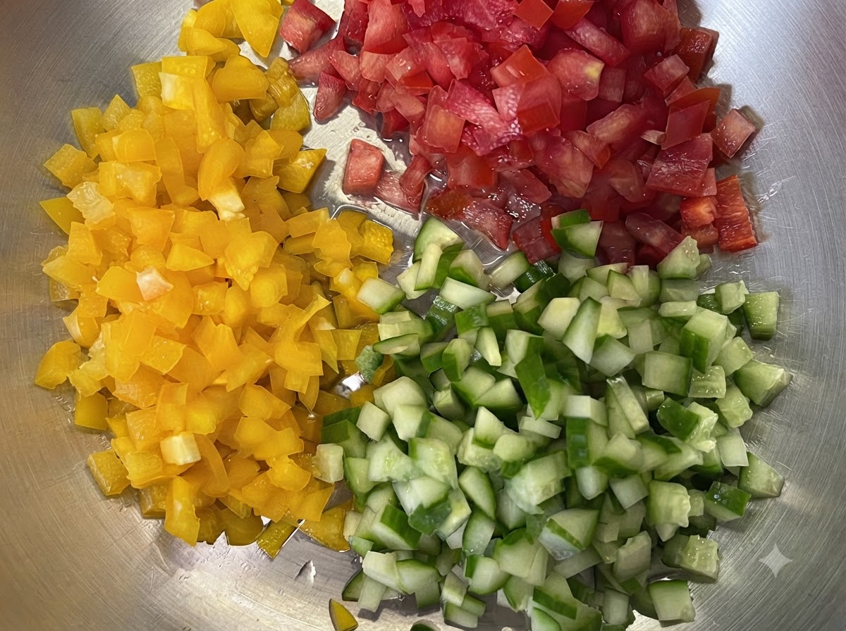 Peperoni gialli, pomodori rossi e cetrioli verdi finemente tagliati a piccoli cubetti su un vassoio.