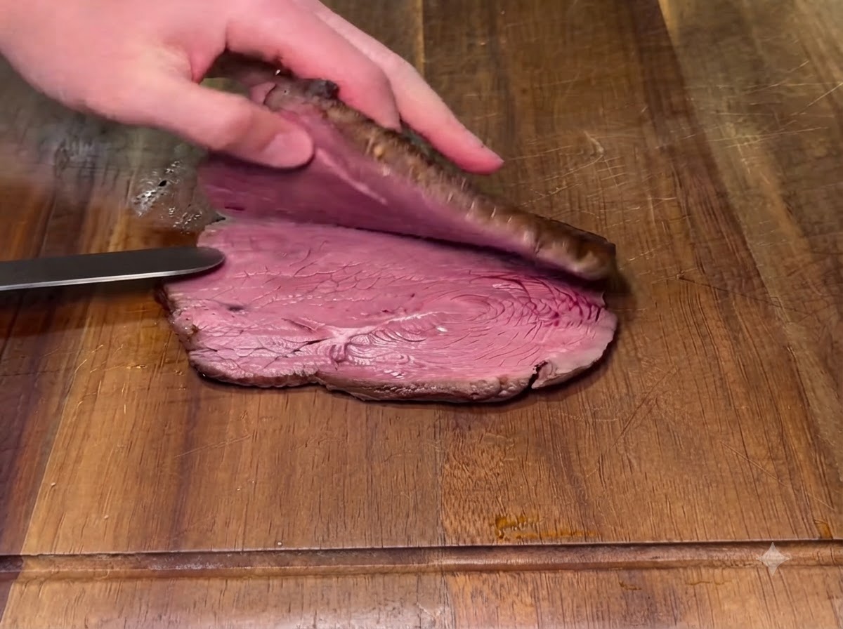 Una bistecca cotta tagliata orizzontalmente a metà su un tagliere di legno con un coltello.