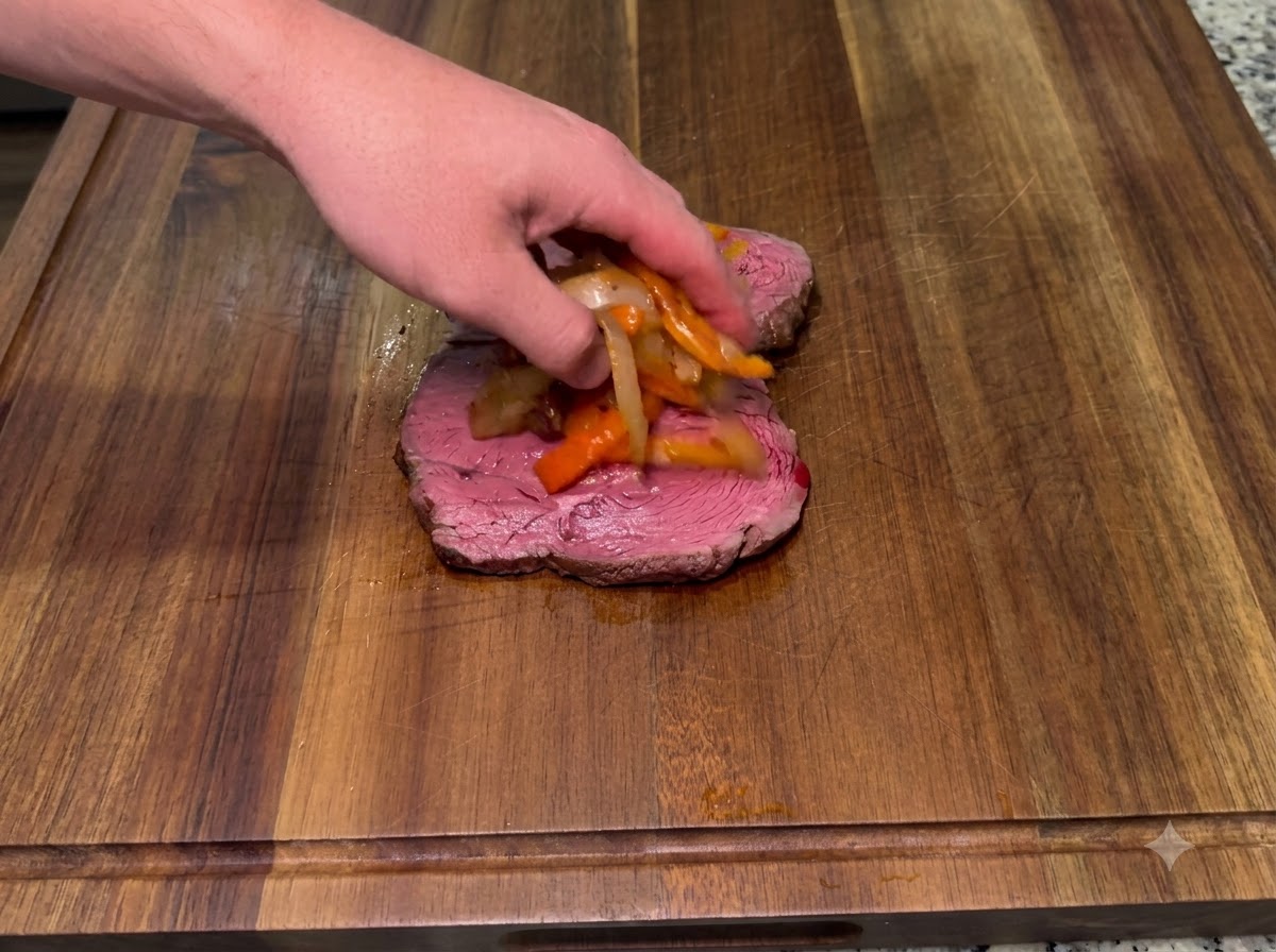 Cipolle saltate e peperoni piccanti affumicati posti sopra un pezzo di bistecca inferiore.