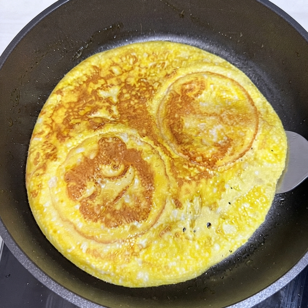 Una spatola che gira uno strato rotondo di uovo cotto e panini da hamburger allinterno di una padella.