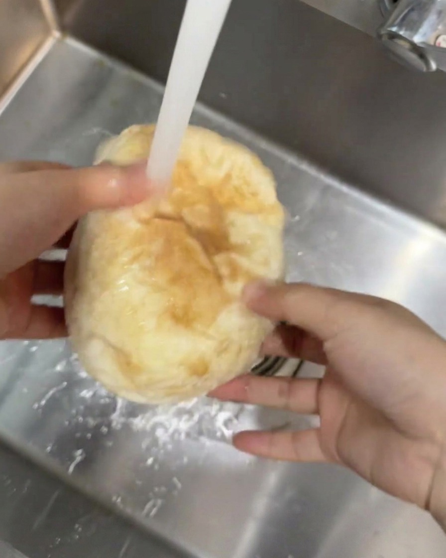 Una pagnotta di ciabatta tenuta sotto un getto di acqua corrente in un lavello da cucina.