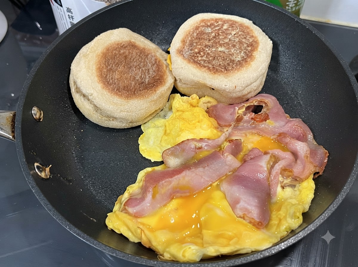 Uova strapazzate in padella con fette di pancetta e muffin inglesi adagiati di lato.