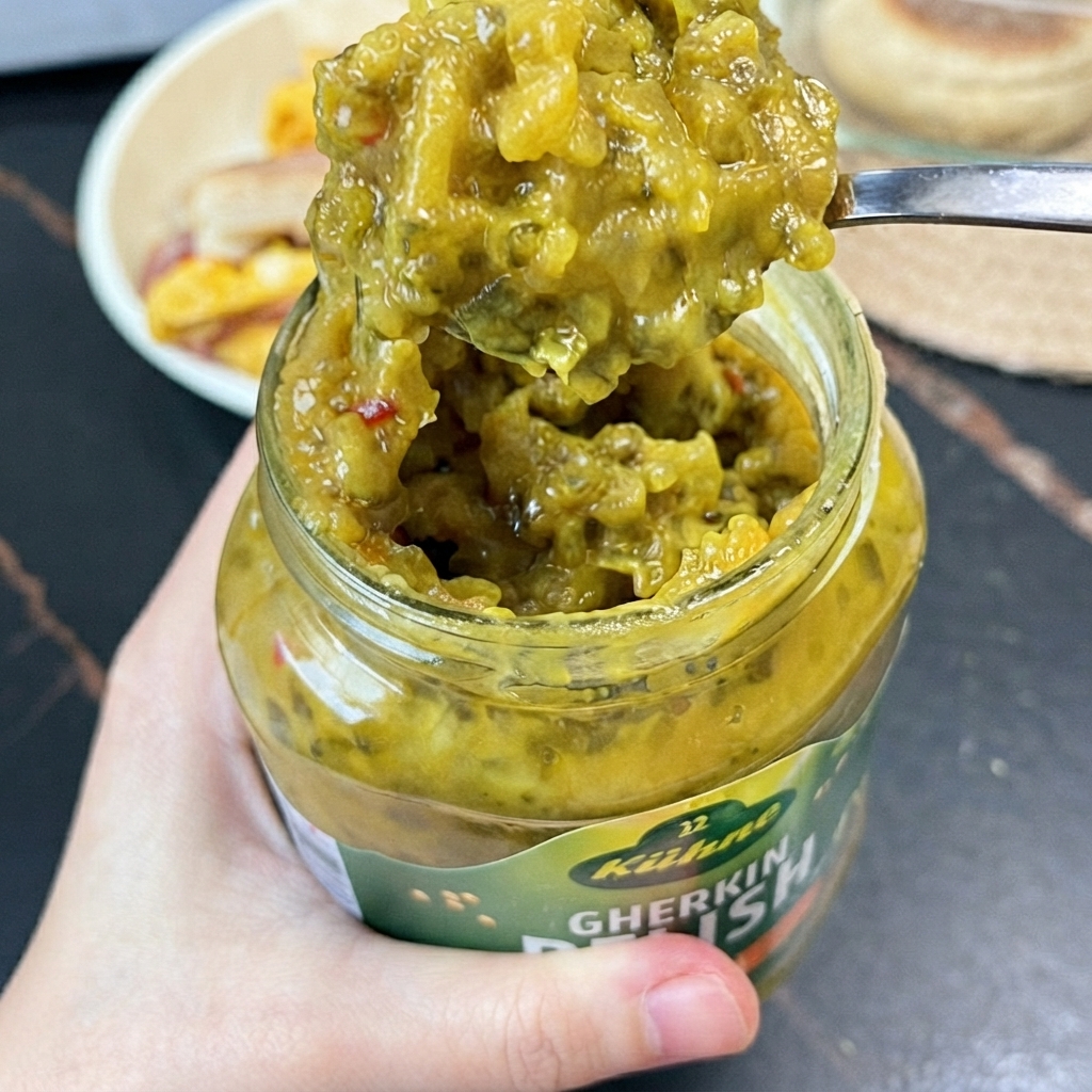 Un cucchiaio di relish di cetriolini verde brillante estratto da un barattolo di vetro con un cucchiaino.