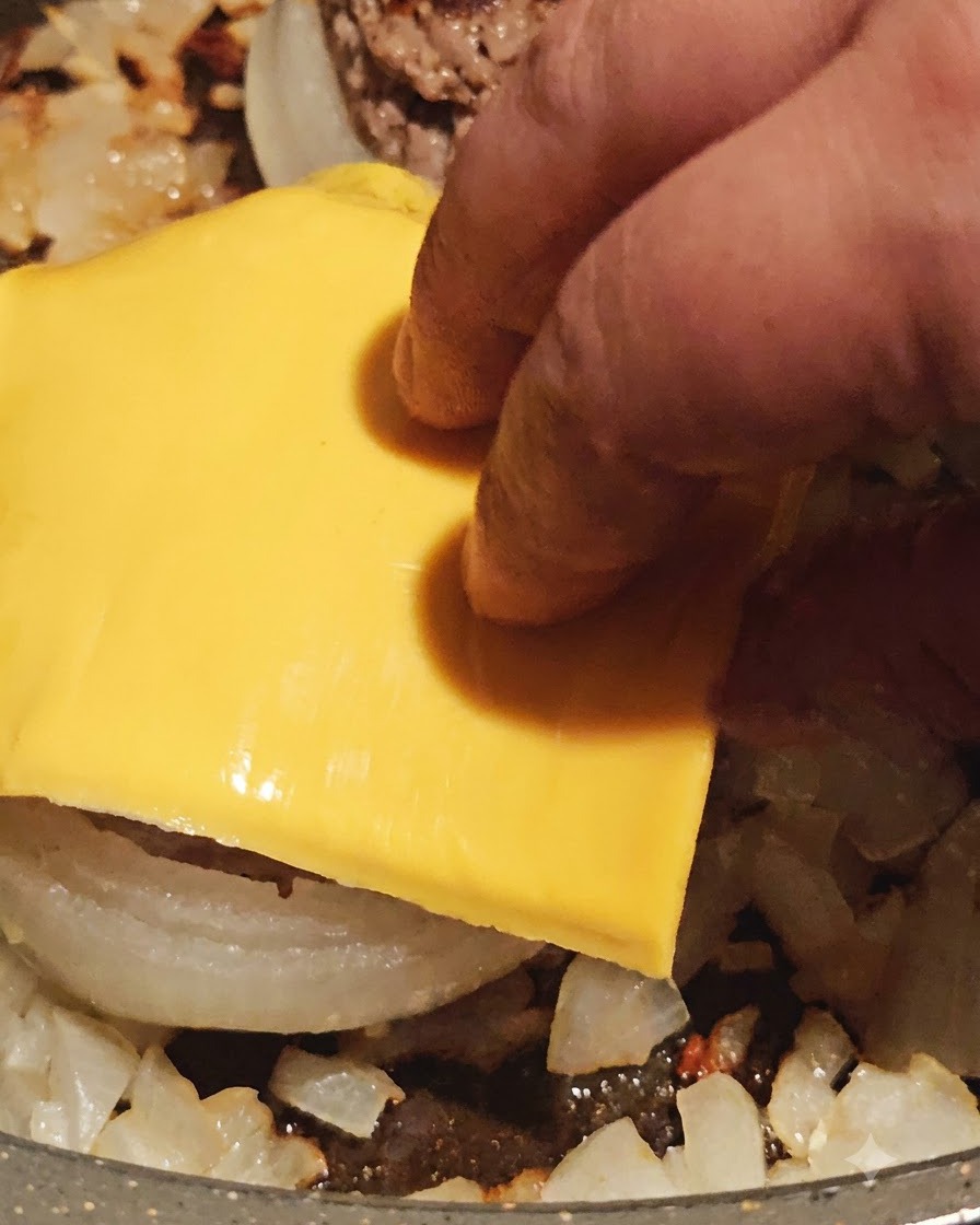Una fetta di formaggio giallo posizionata sopra un anello di cipolla ripieno di carne cotta nella padella.