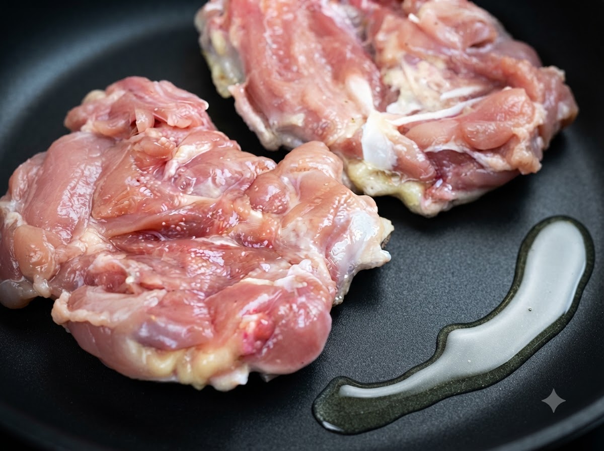 Due cosce di pollo crudo adagiate in una padella accanto a una pozza di olio da cucina.