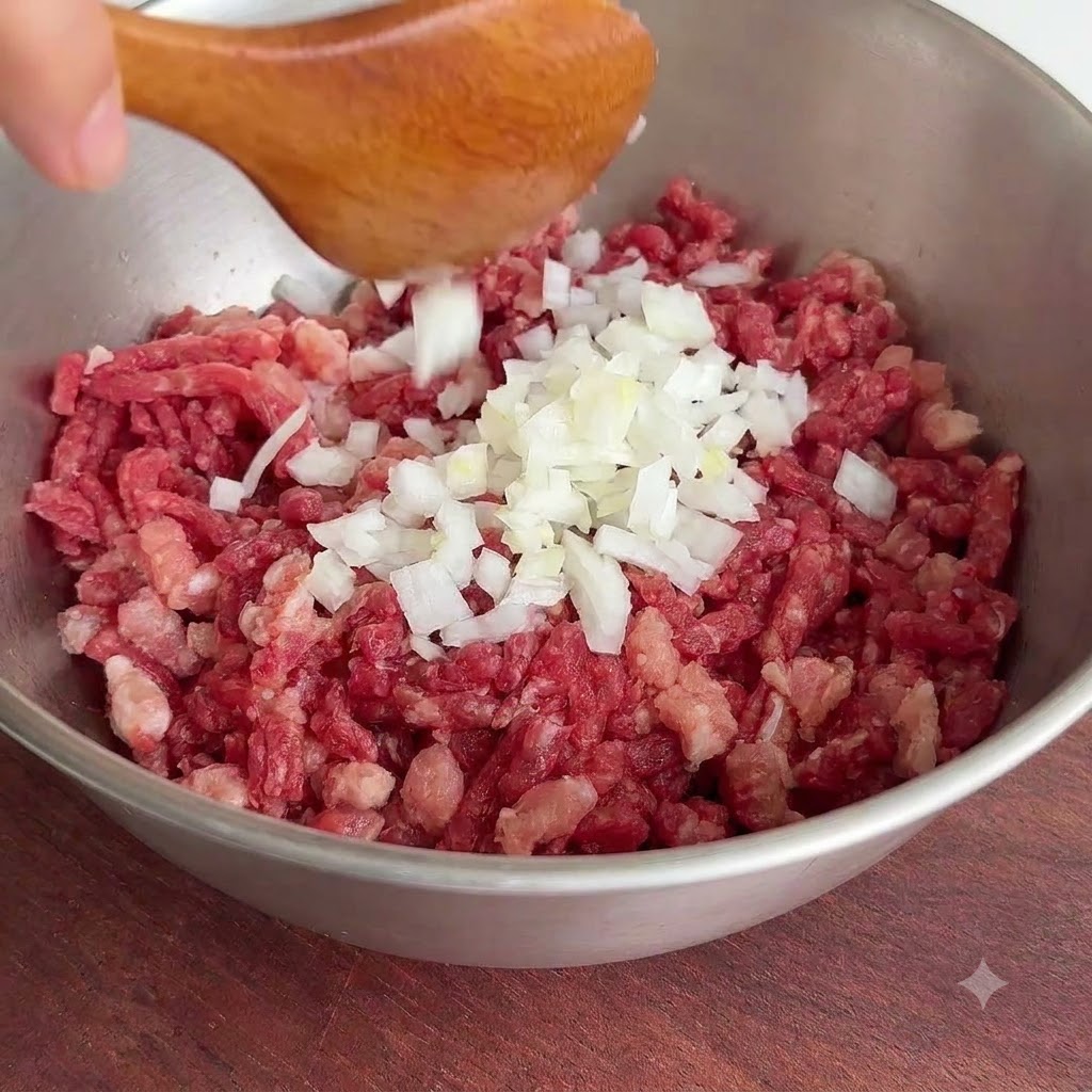 Un mucchio di pezzi di cipolla bianca fresca fatti cadere da un cucchiaio di legno in una ciotola di metallo con carne di manzo cruda macinata.