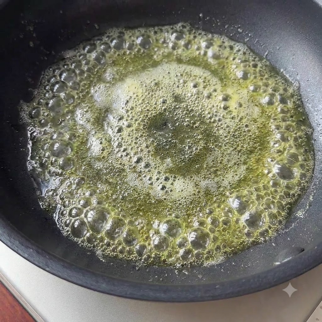 Un piccolo pezzo di burro che si scioglie e bolle in una padella nera.
