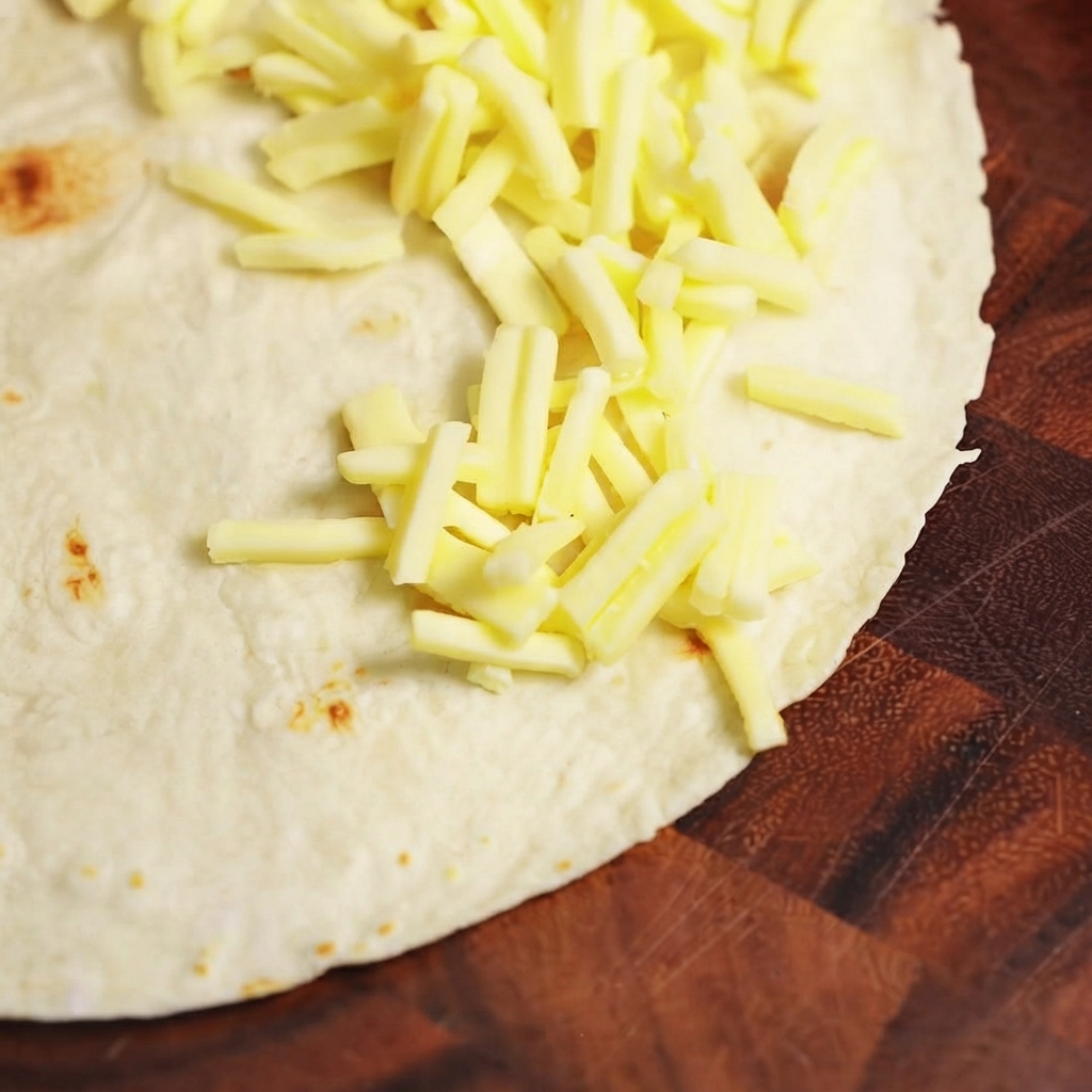 Ripieno di manzo cotto e formaggio mozzarella disposti su una metà di una tortilla di grano piatta.