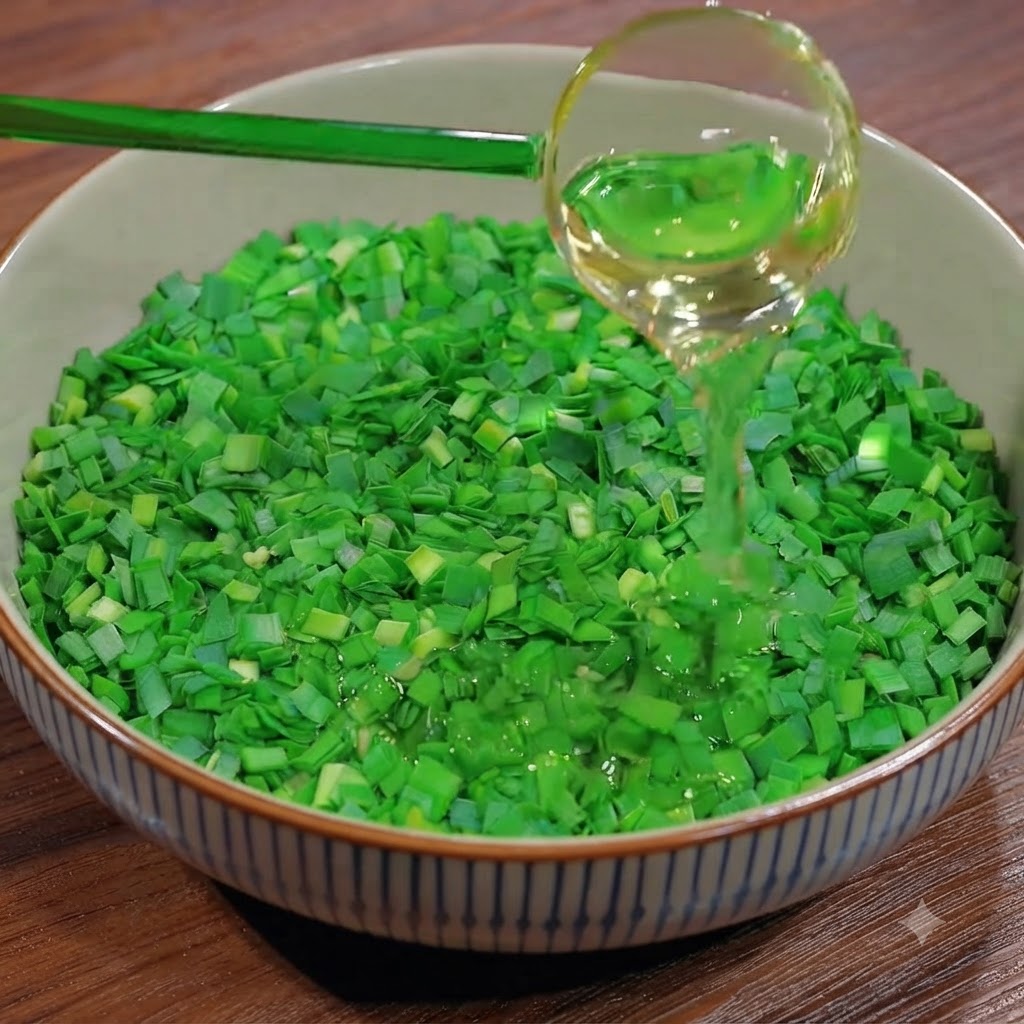 Un mestolo che versa olio da cucina su una ciotola riempita di erba cipollina verde fresca tritata.