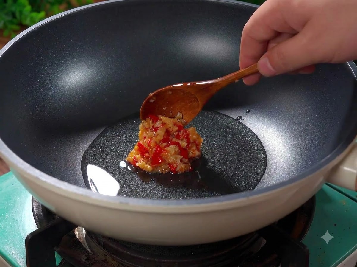 Aglio tritato e peperoncini rossi tagliati a pezzi che sfrigolano nellolio caldo allinterno di un wok.