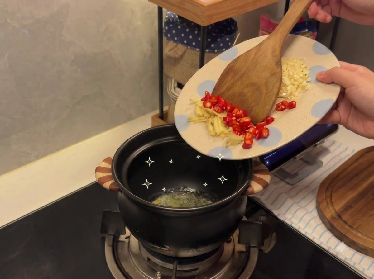 Aglio tritato e peperoncini trasferiti da un piatto decorato nel tegame in ceramica con il burro fuso.