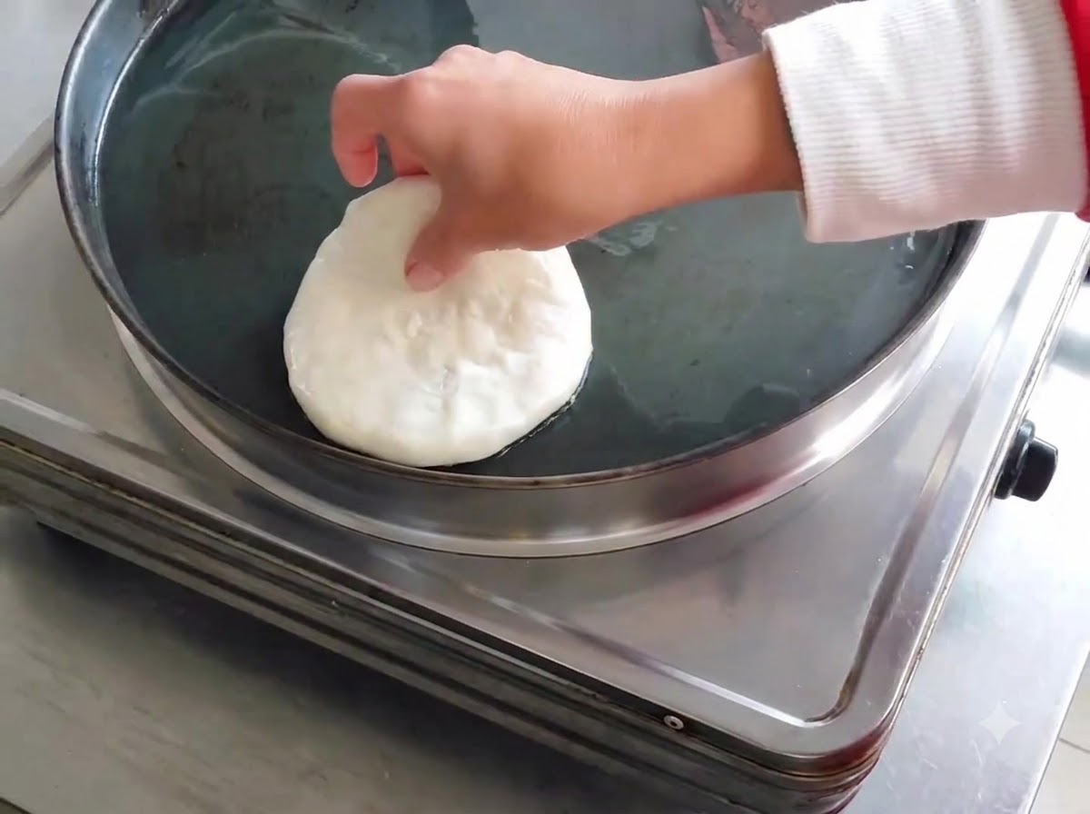 Un panzerotto di carne crudo e modellato che viene messo in una padella elettrica oliata.