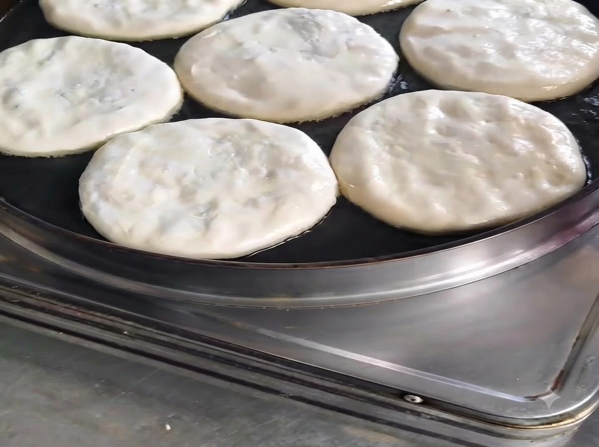 Diversi panzerotti di carne rotondi che cuociono in una padella con olio irrorato sopra.