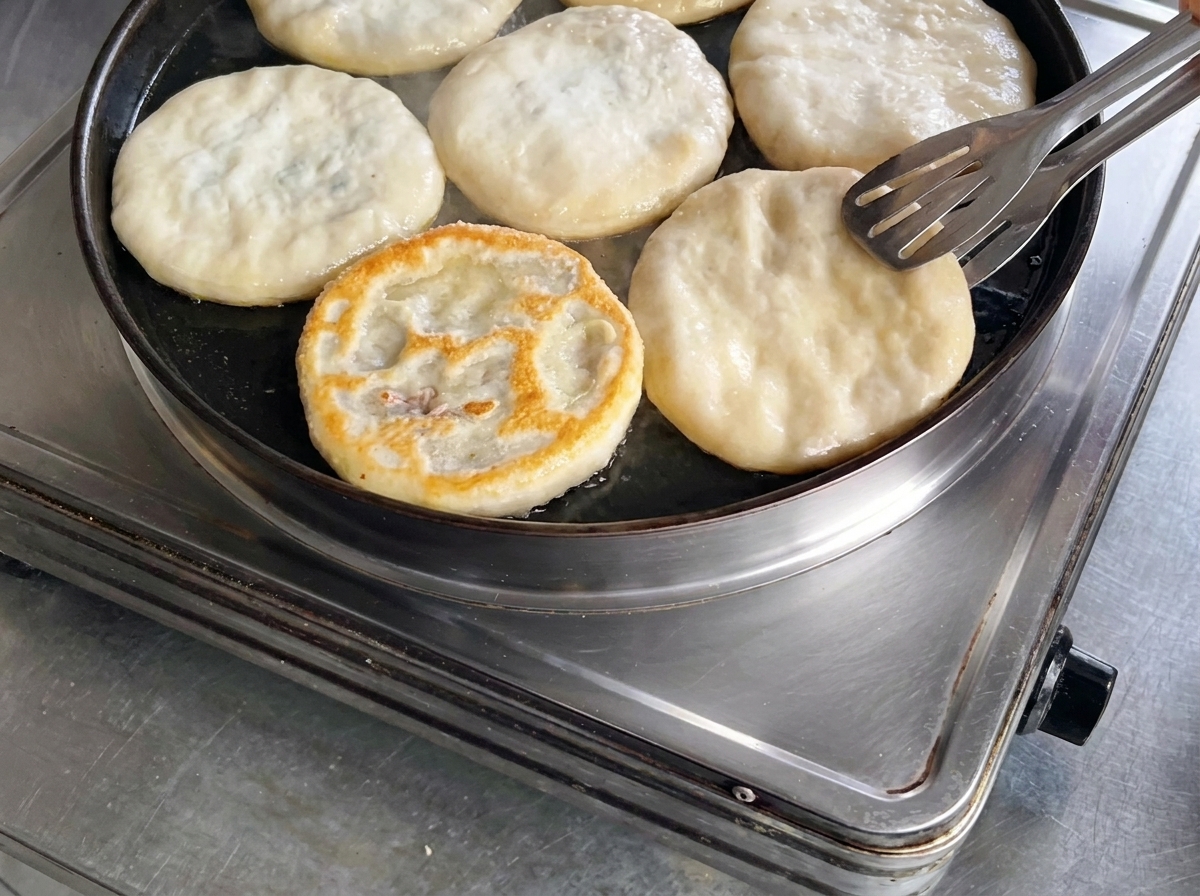 Luso di pinze da cucina in metallo per girare un panzerotto di carne in una padella, rivelando una superficie superiore perfettamente dorata e croccante.