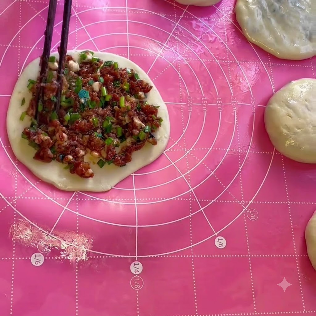 Ripieno di carne ed erba cipollotica distribuito uniformemente su un foglio circolare di impasto usando le bacchette.
