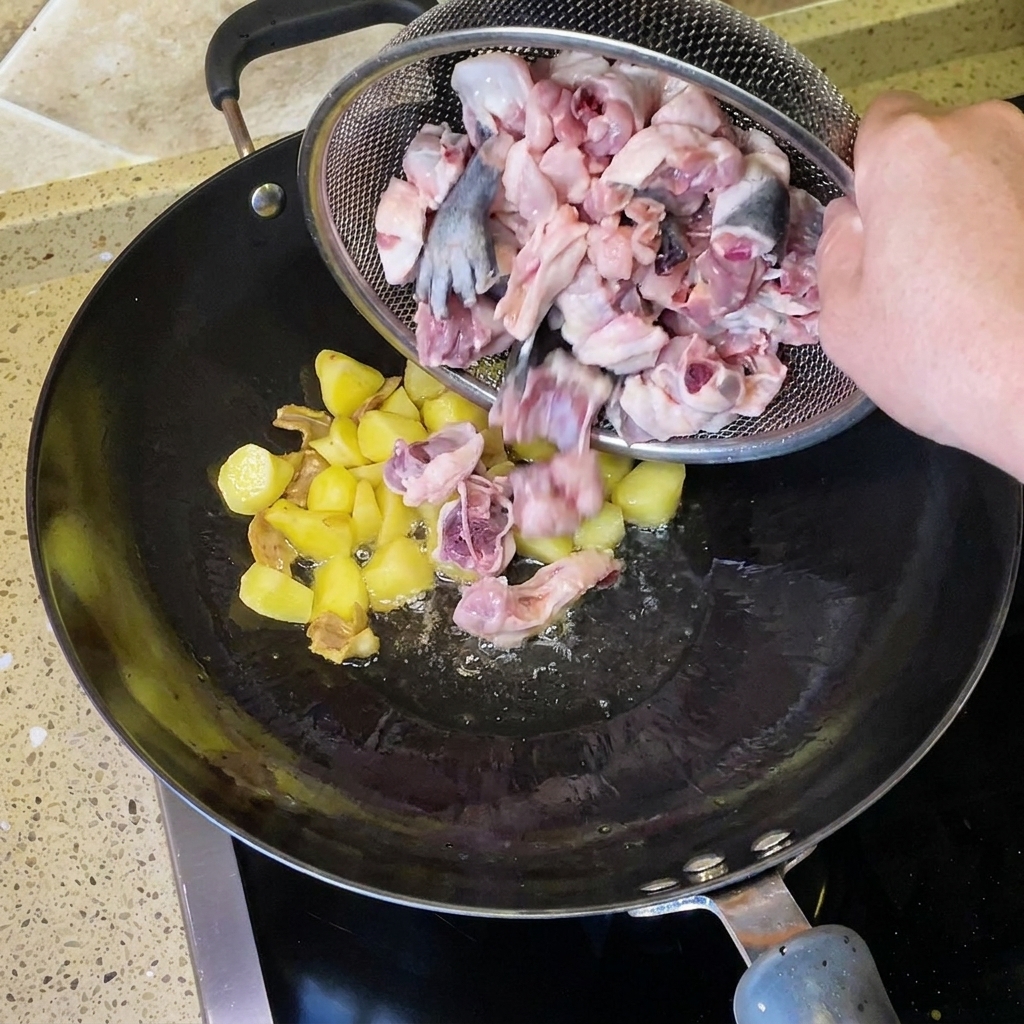 Pezzi di pollo crudo tagliati a pezzi versati da un colino nel wok con lo zenzero.