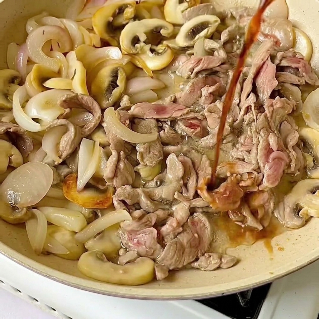 Salsa di soia leggera versata dallalto su fette di manzo crudo e verdure cotte in padella.