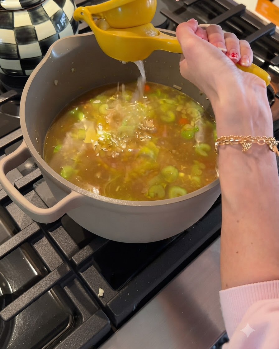 Spremitura di succo di limone fresco da uno spremiagrumi giallo in una pentola di brodo di pollo e verdure in ebollizione.