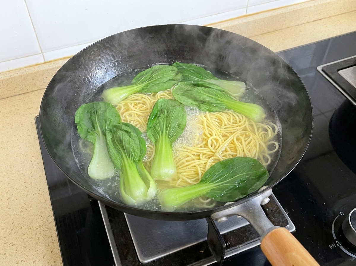 Foglie di bok choy fresco che galleggiano nellacqua bollente insieme ai noodle in ebollizione in un wok.