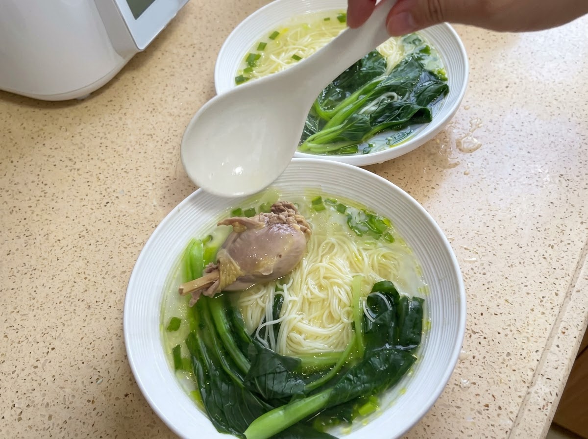 Una ciotola di noodle guarnita con un pezzo di pollo e bok choy cotto.