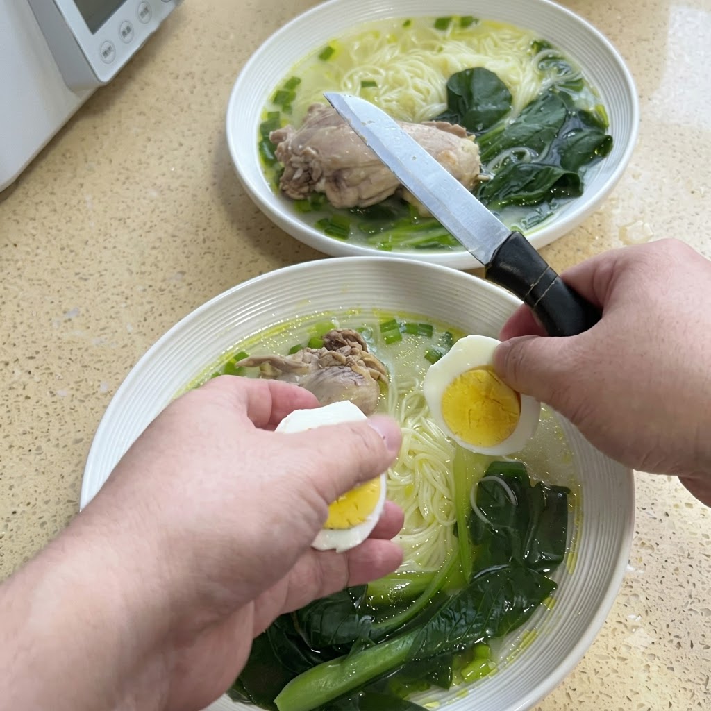 Mani che tagliano a metà un uovo sodo con un coltello sopra una ciotola di noodle in brodo.
