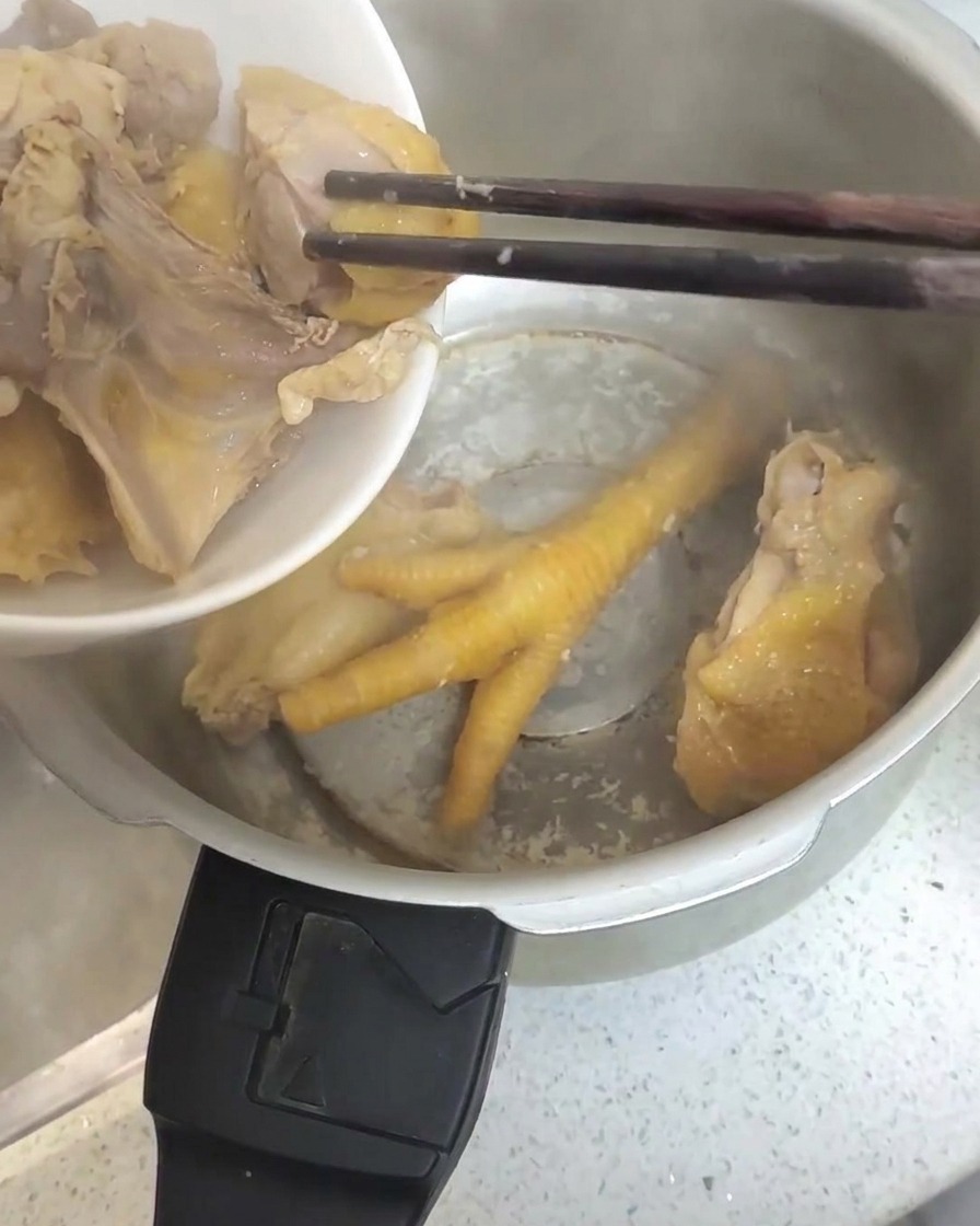 Pezzi di pollo sbollentati trasferiti con le bacchette in una pentola a pressione in acciaio inossidabile.