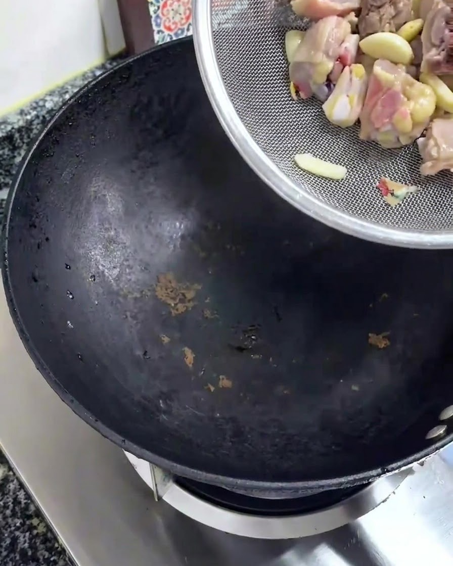Pezzi di pollo crudo tagliati versati da un colino dargento in un wok nero.