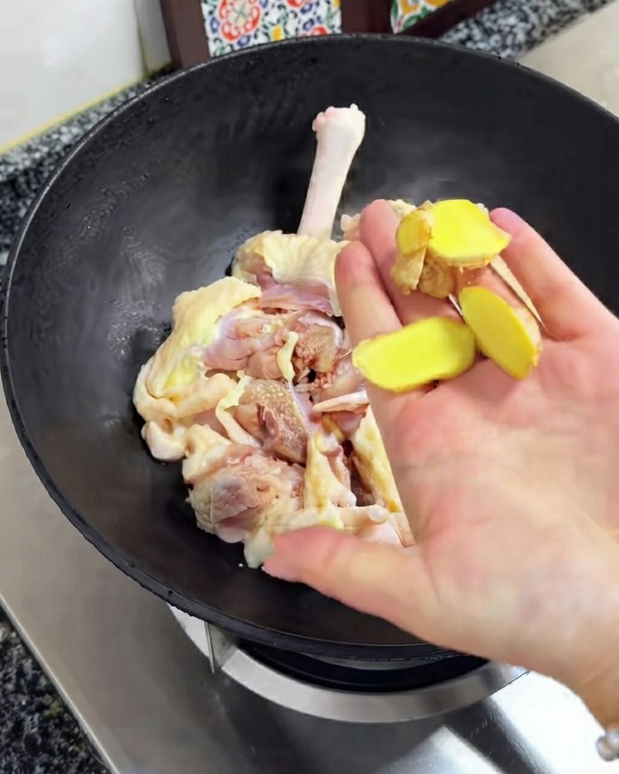Fette di zenzero fresco tenute sopra il pollo crudo allinterno del wok nero.