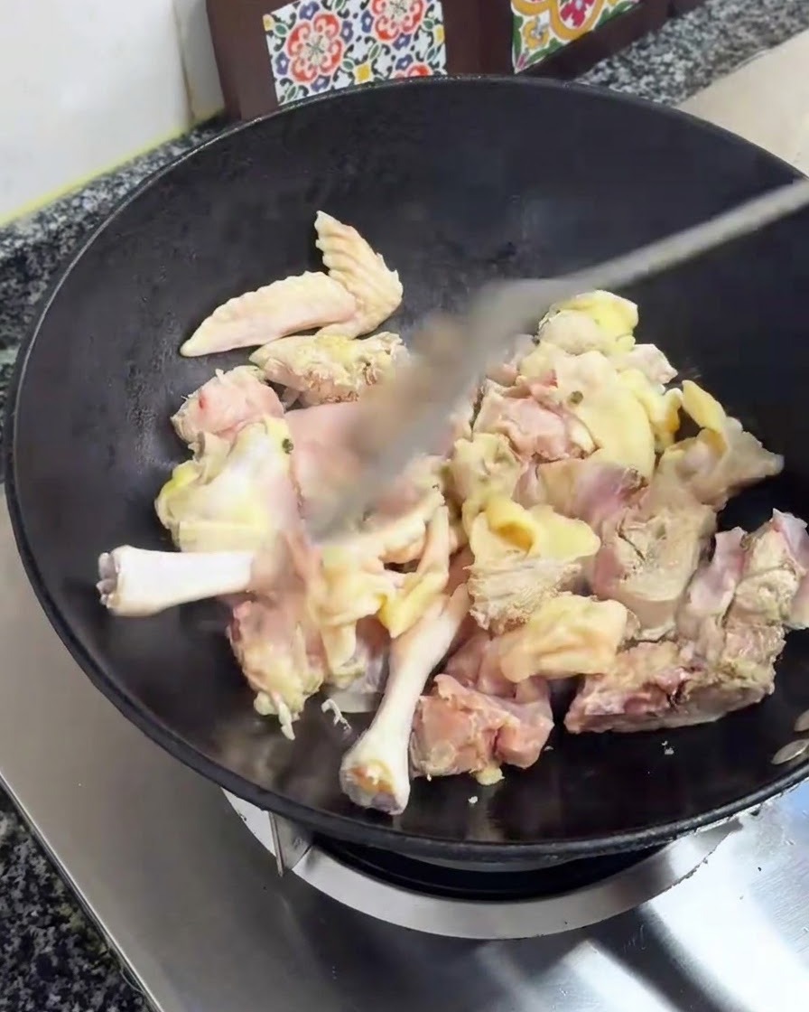Pezzi di pollo saltati con una spatola in un wok nero sopra un fornello.