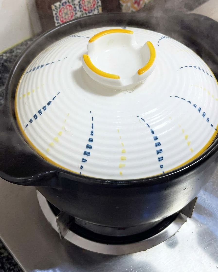 Un coperchio bianco con motivi blu e gialli posizionato saldamente sopra una pentola di terracotta nera.