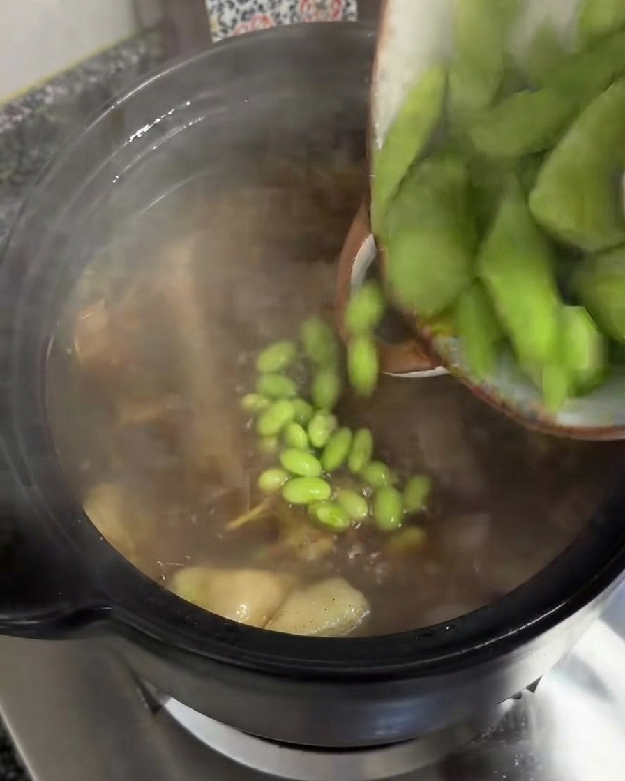 Fette spesse di celtuce verde versate da una ciotola in una pentola di zuppa sobbollente.
