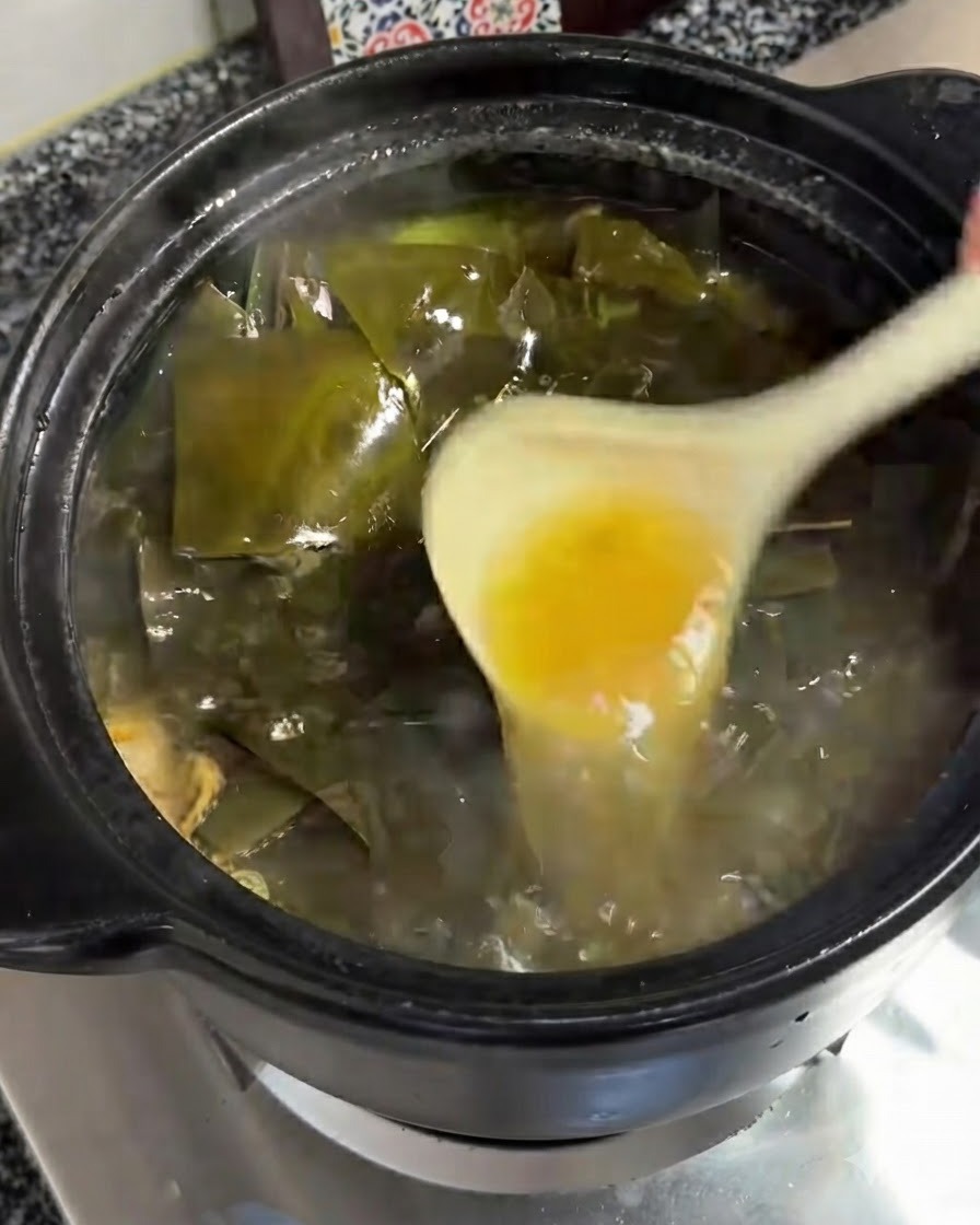 Un mettolino che rimuove uno strato di olio giallastro dalla superficie ribollente della zuppa.