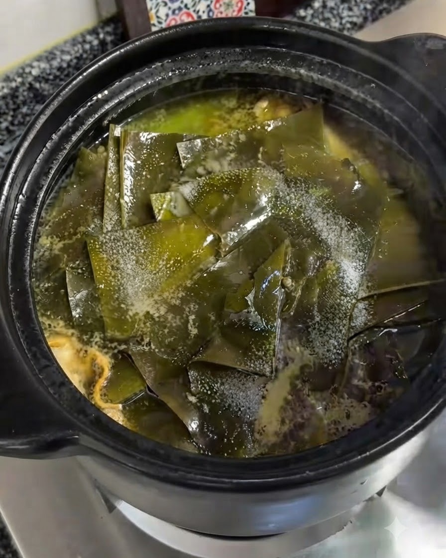 Sale fino spruzzato direttamente sopra i pezzi di alga kelp verde che galleggiano nella pentola di terracotta sobbollente.