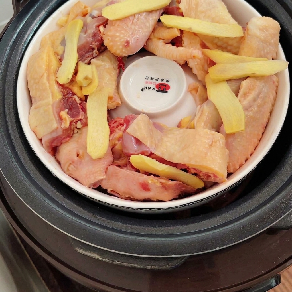 Fette di zenzero fresco adagiate sopra i pezzi di pollo allinterno della pentola.