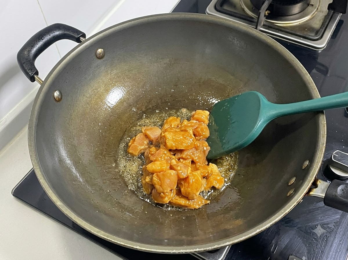 Petto di pollo marinato a dadini saltato in un wok riscaldato con una spatola verde.