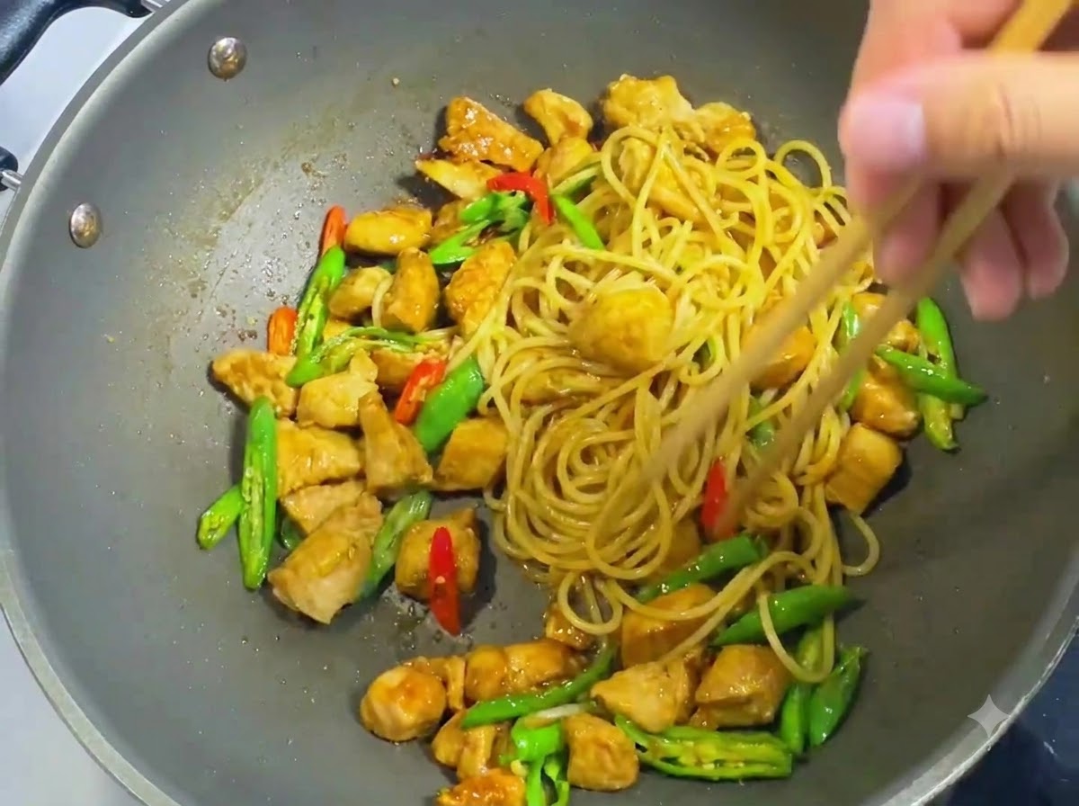 Bacchette di legno che mescolano e uniscono uniformemente spaghetti, pollo a dadini, peperoncini affettati e salsa scura in un wok.