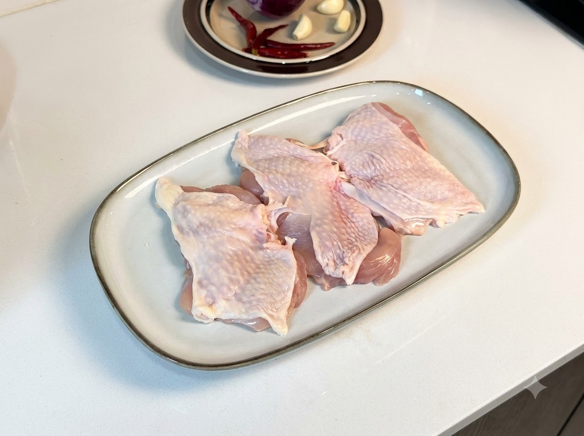 Cosce di pollo disossate disposte su un piatto bianco rettangolare, cosparse di pepe nero e condimenti.