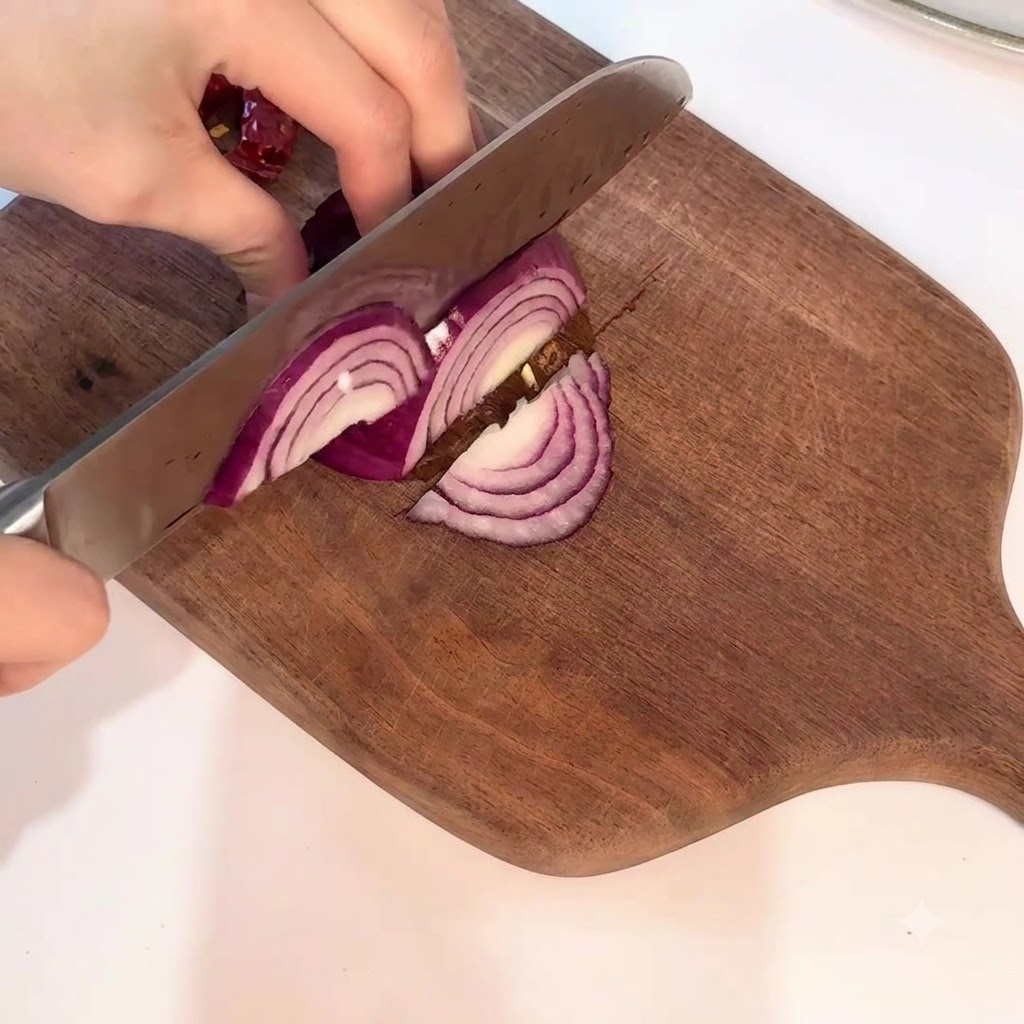 Una cipolla rossa tagliata accuratamente con un coltello in nette sezioni a mezzaluna su un tagliere.