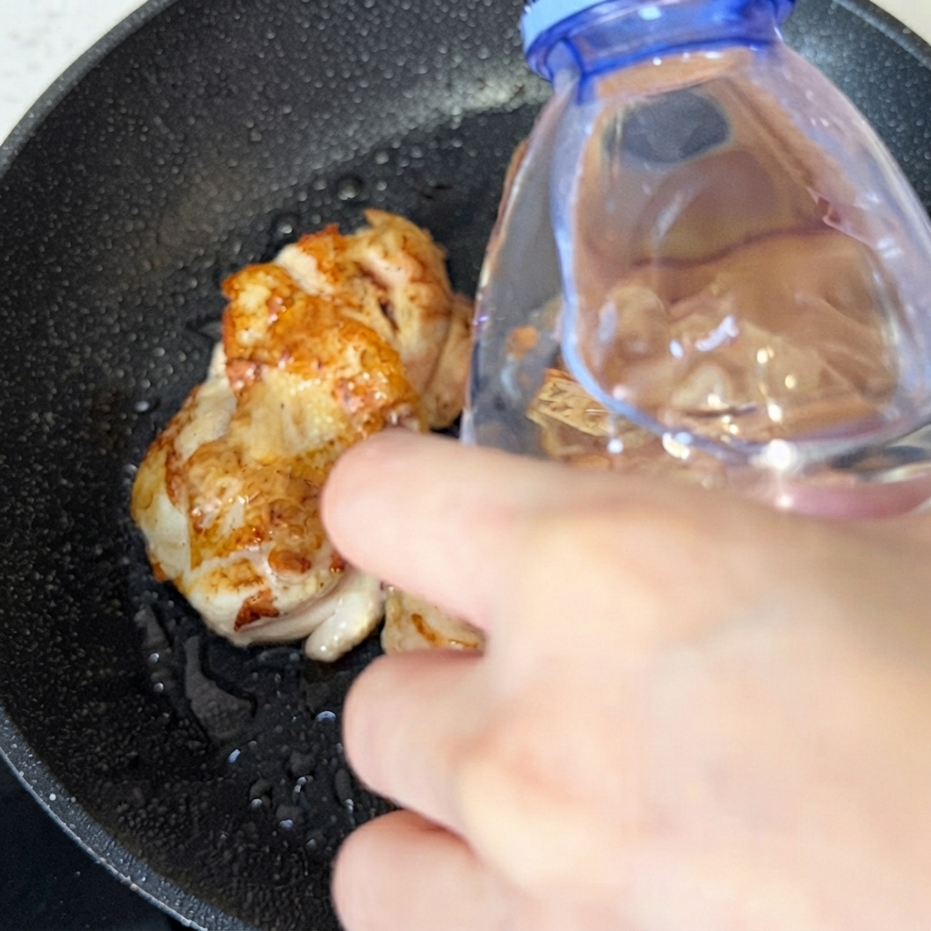 Una bottiglia dacqua che versa una piccola quantità dacqua nella padella sopra i pezzi di pollo cotto.