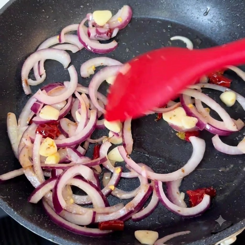 Fette di cipolla rossa, aglio e peperoncini secchi saltati in una padella calda con una spatola in silicone rosso.
