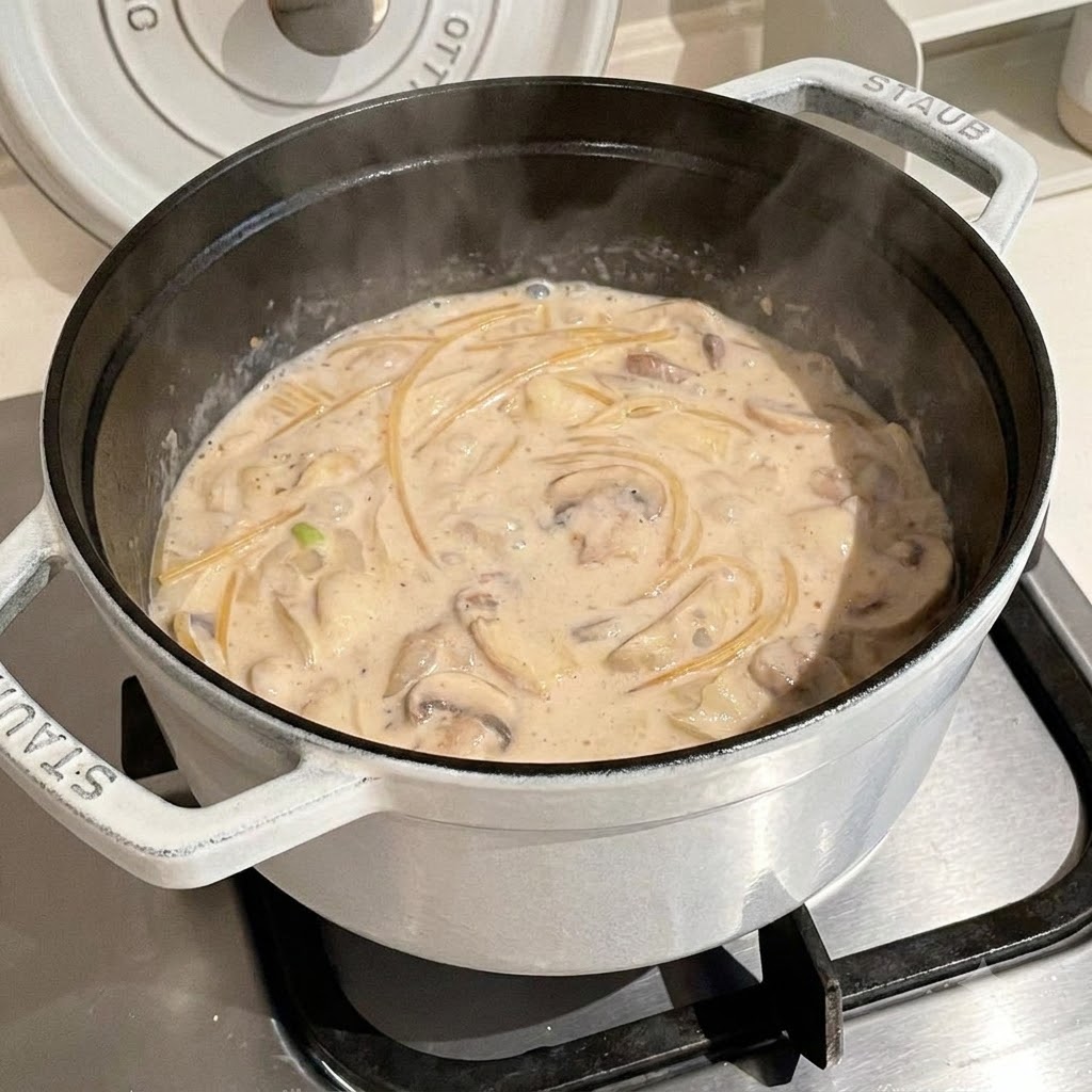 Spaghetti in cottura allinterno di un brodo cremoso e fumante dentro una pentola bianca.