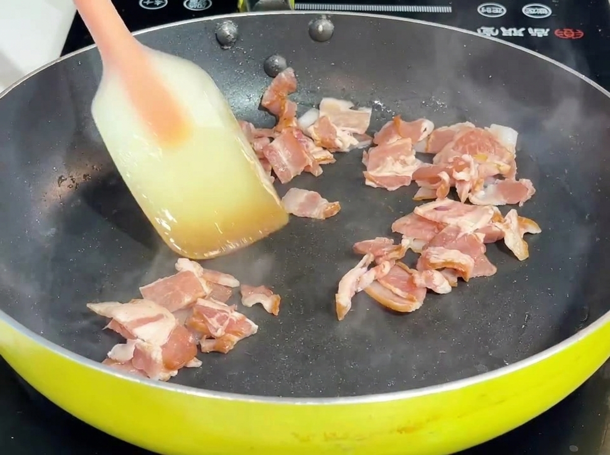 Pancetta e cipolla saltate in padella con una spatola.