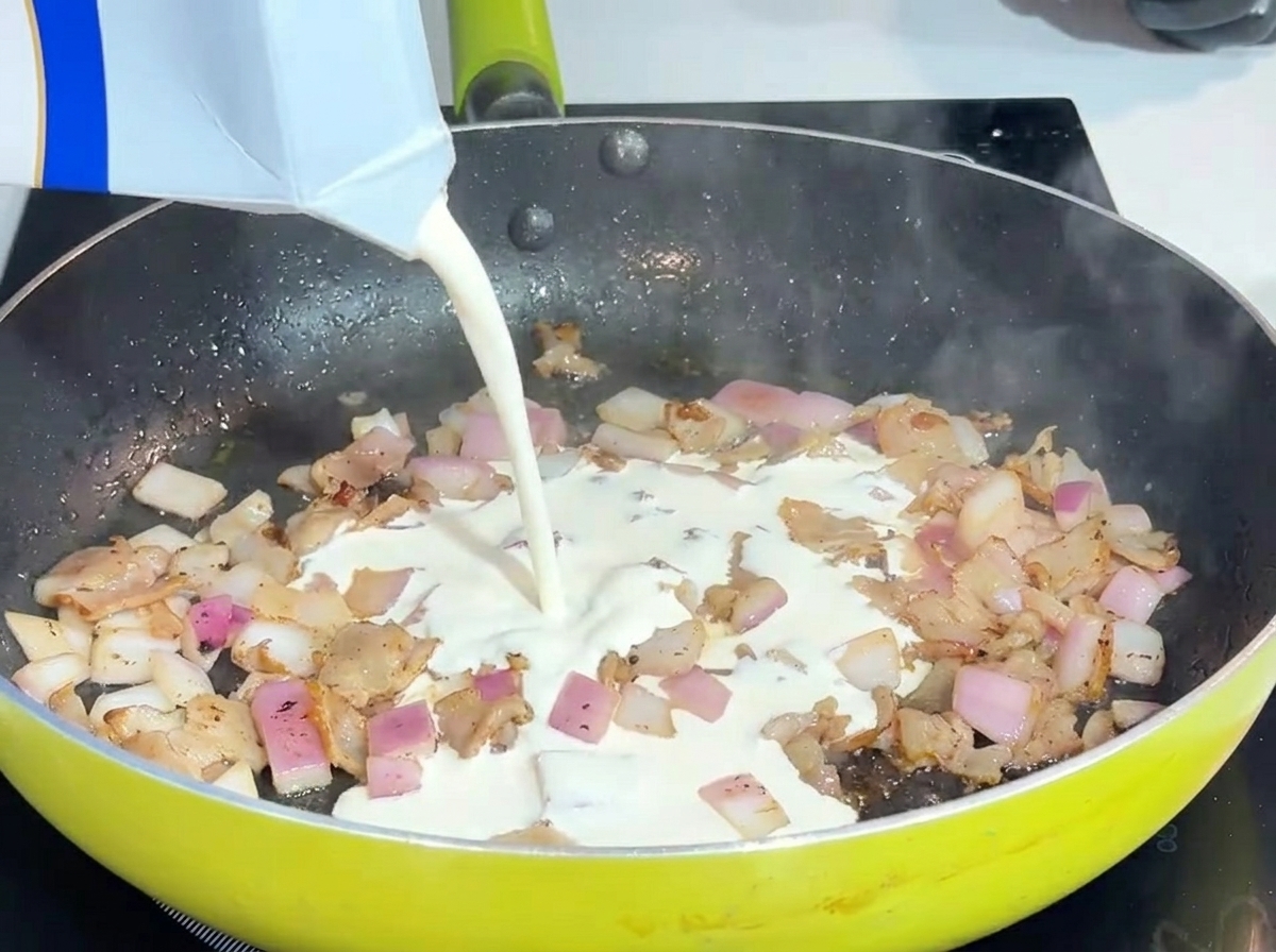 Panna fresca liquida versata in una padella con pancetta e cipolle.