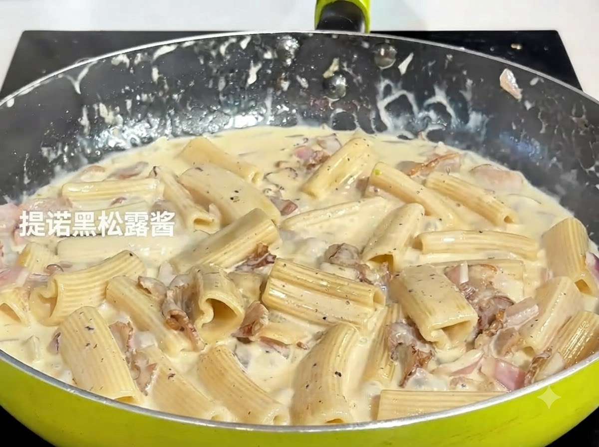 Un cucchiaio di pasta di tartufo nero scuro aggiunto al composto di pasta che sobbolle in padella.