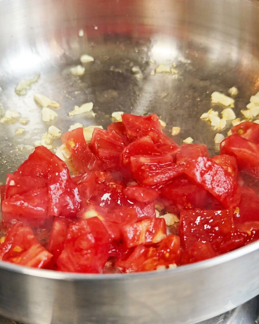 Pomodori rossi freschi a dadini saltati con aglio allinterno di una padella di metallo.