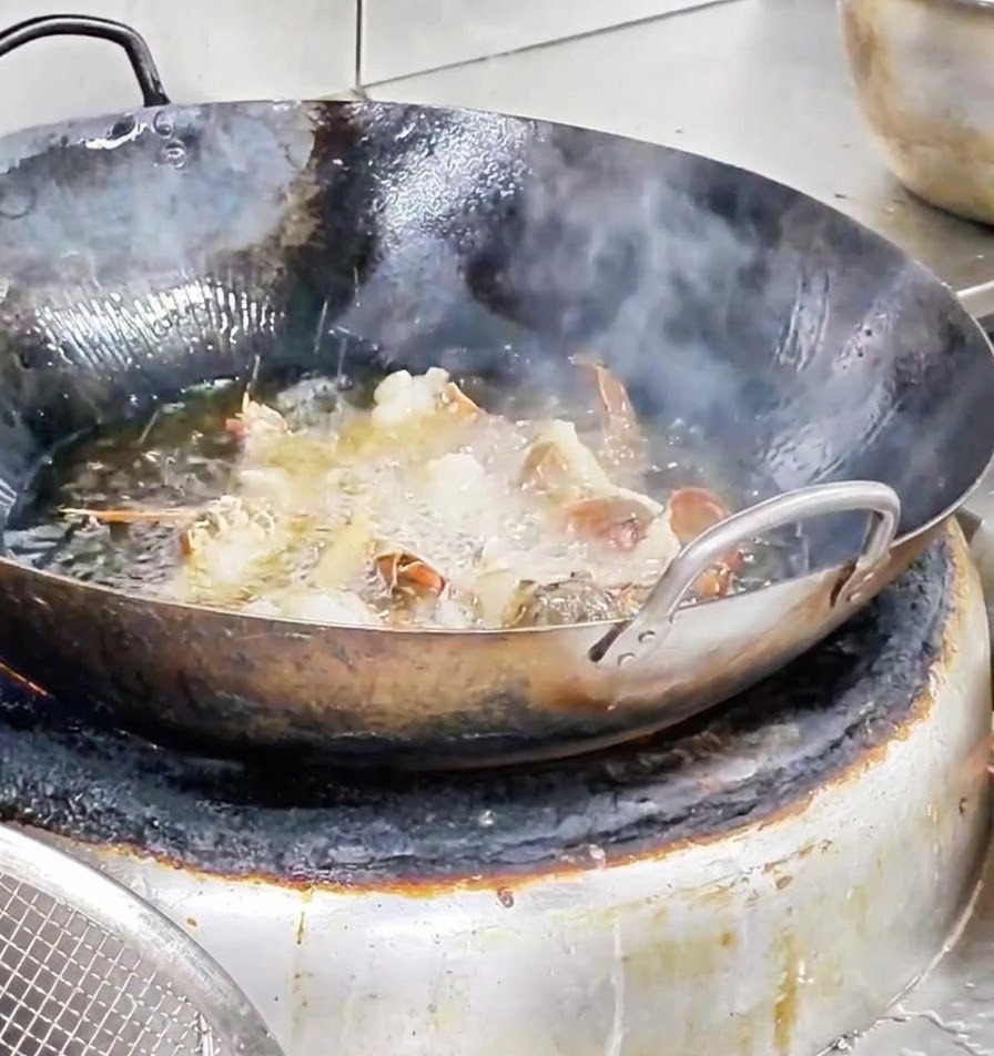 Pezzi di aragosta che friggono vigorosamente in un wok pieno di olio bollente.