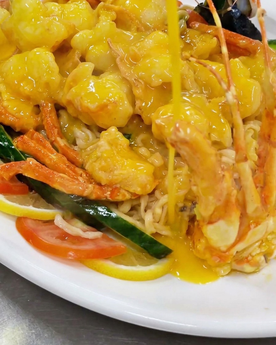 Versamento dei pezzi di aragosta fitta in un wok pieno di una ricca salsa gialla al formaggio bollente.