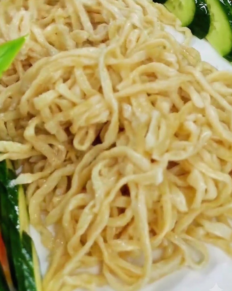 Disposizione dei pezzi di aragosta cotta sopra il letto di noodles su un piatto da portata bianco.
