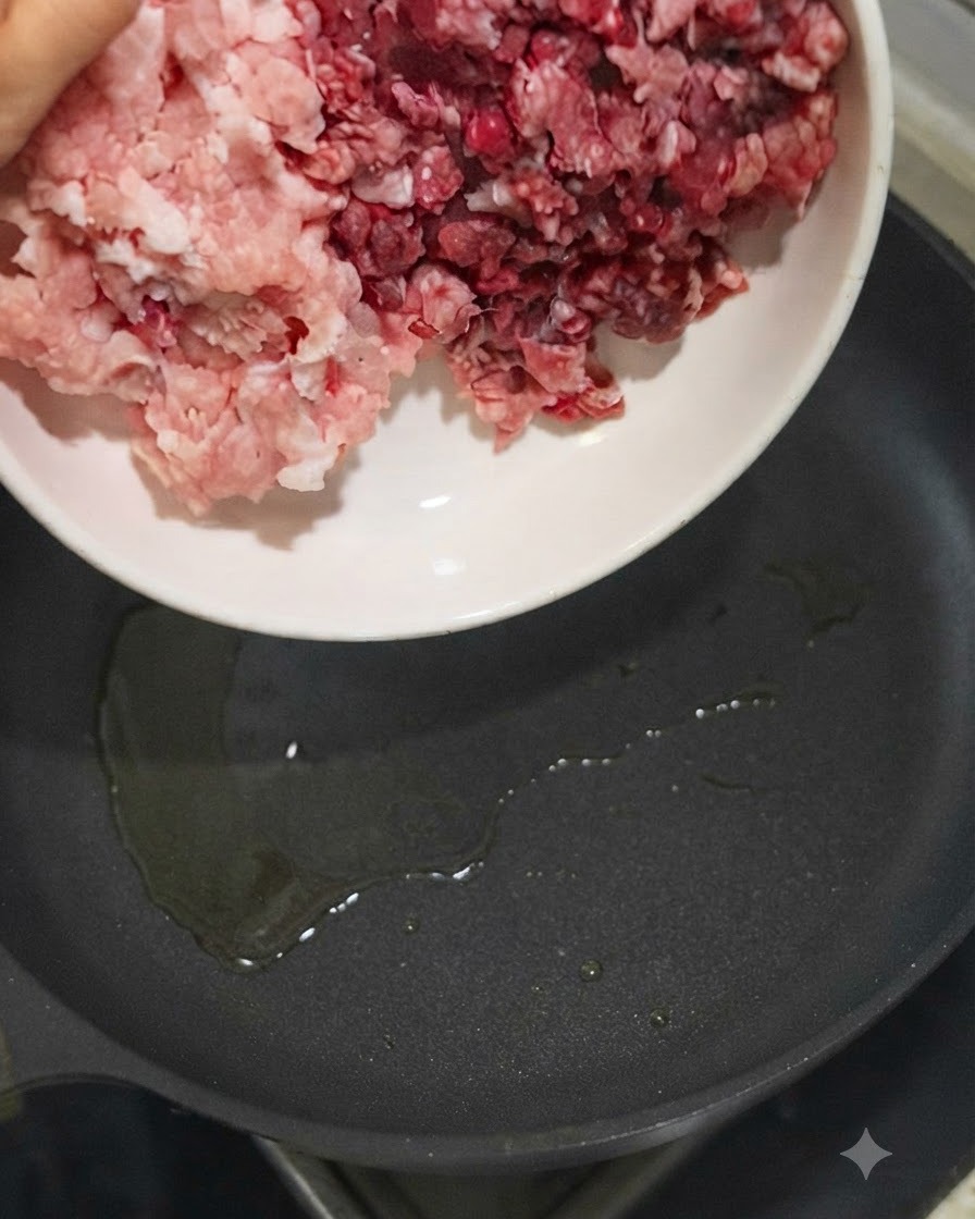 Carne di maiale e di manzo macinata versata da una ciotola bianca in una padella calda con olio.